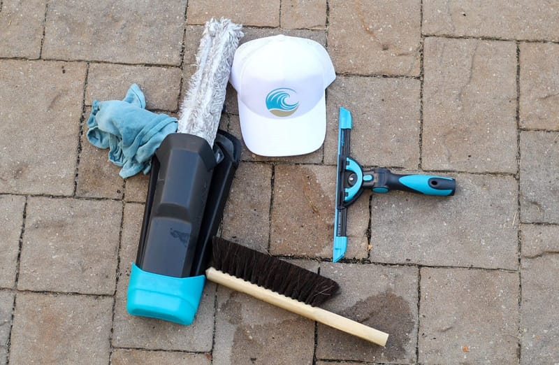 Cove Cleaning window tools laid out on pavers: scrubber, squeegee, brush, and branded cap